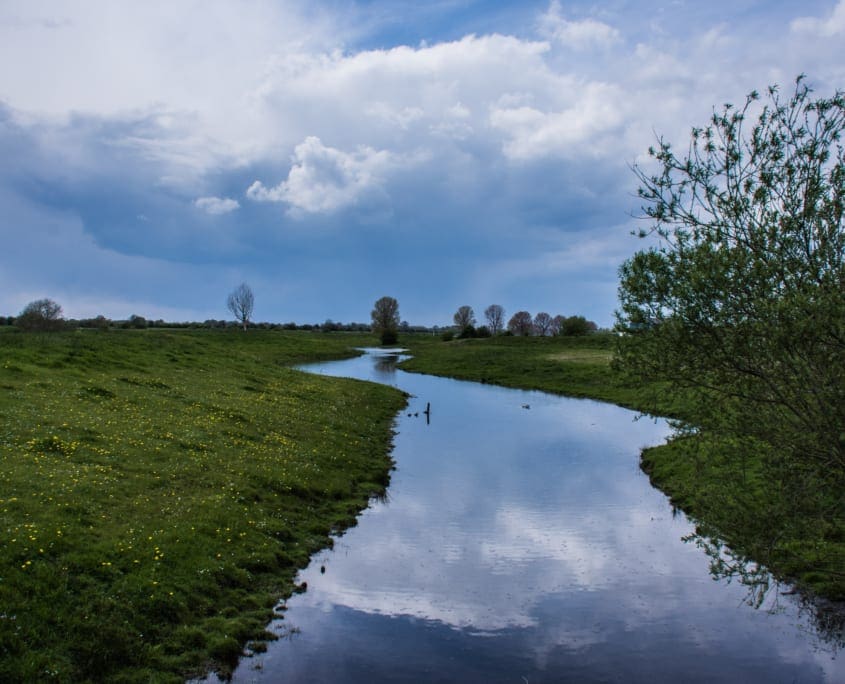 De omgeving van het Genneperhuis: de Niers, akkers en Oudhollandsche wolkenpartijen.